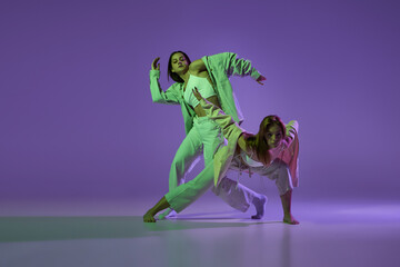 Experimental dance. Two young girl in motion, action isolated over purple background. Emotions, love, style, youth, music and fashion