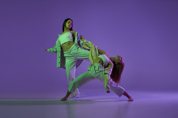 Experimental dance. Two young girl in motion, action isolated over purple background. Emotions,...