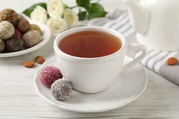 Cup of aromatic tea and delicious vegan candy balls on white wooden table