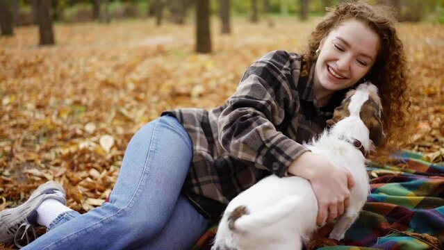 Curly woman laying on a plaid with her jack russell terrier puppy in autumn park