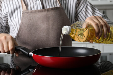 Woman pouring cooking oil from bottle into frying pan on stove, closeup