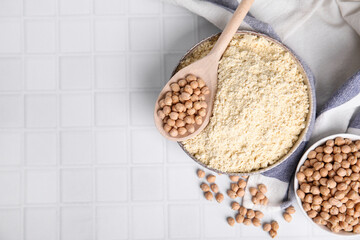 Chickpea flour in bowl and seeds on white tiled table, flat lay. Space for text