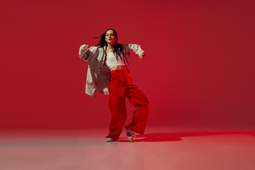 Dynamic portrait of young girl dancing hip-hop or contemporary dance isolated on dark red...