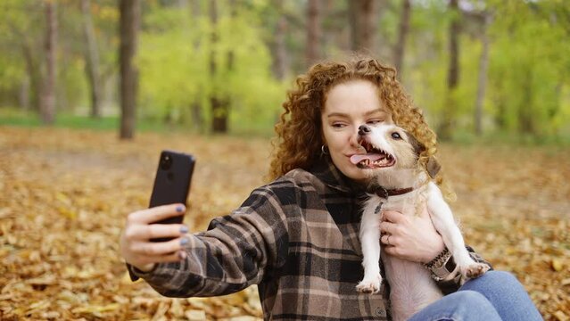Smiling young woman with dog outdoors in autumn making selfie