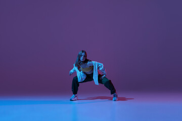 Fototapeta na wymiar Flexible young girl, contemp dancer dancing hip-hop or experimental dance isolated on dark purple background in neon. Contemporary dance. Music, dance, active lifestyle, fashion, style