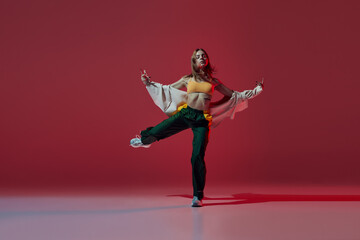 Dynamic portrait of young girl dancing hip-hop or contemporary dance isolated on dark red background. Experimental dance. Music, dance, active lifestyle, fashion, style