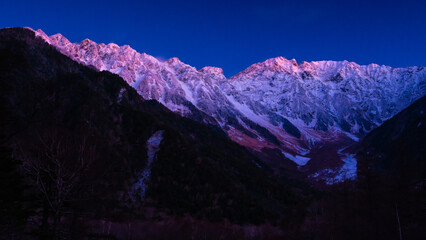 北アルプスの山脈に薄らの雪景色、薄暗い朝焼けによるピンク色に染まる。