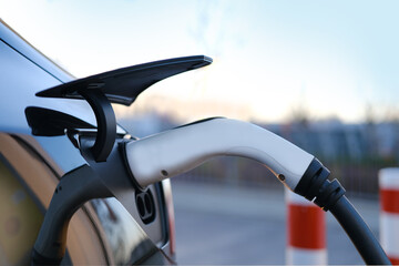 close-up adapter with electric vehicle cables, part of black car charging energy, replenish battery...