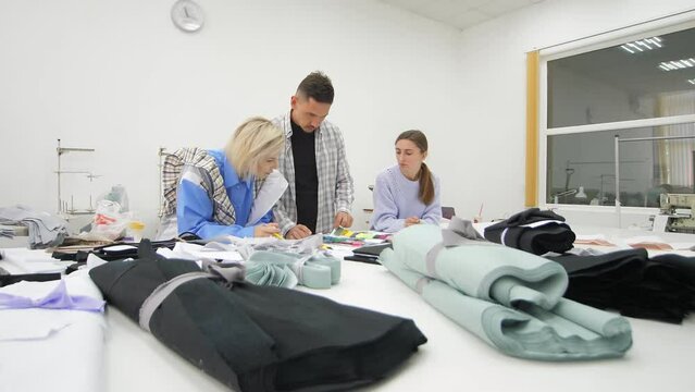 Group of three diverse fashion dressmakers looking at fabric samples and discussing ideas for garments in the atelier studio. Small business and dressmaking concept. Garment making industry.