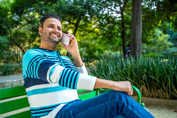 Young indian man talking on smartphone at park.