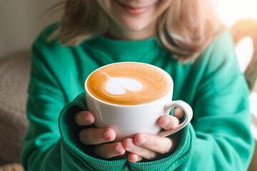 Beautiful girl in green sweater holding cup of tea or coffee in the morning. Closeup of female...