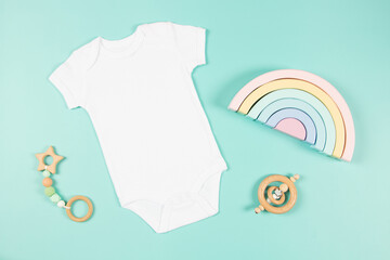 White cotton baby short sleeve bodysuit and natural wooden toy on light green background. Infant...