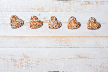 Sweet heart-shaped glazed gingerbread photographed on a white wooden surface.