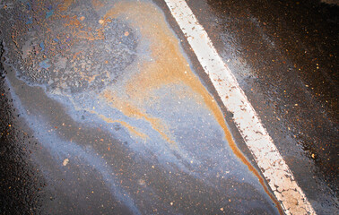 Oil spill on dark asphalt, parking lot with dividing lines.