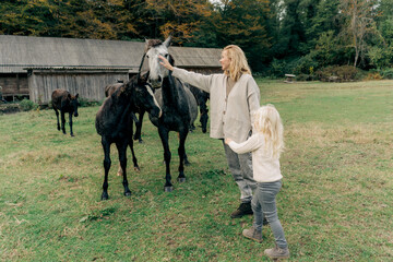 Mom and daughter walk around the farm and stroke the horses.