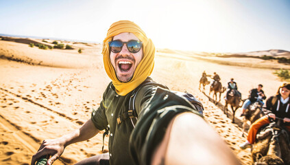 Happy tourist having fun enjoying group camel ride tour in the desert - Travel, vacation activities and adventure concept