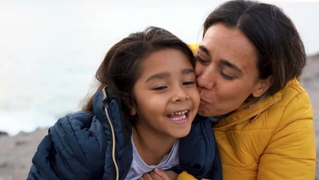 Happy latin mother kissing little daughter outdoor during winter time