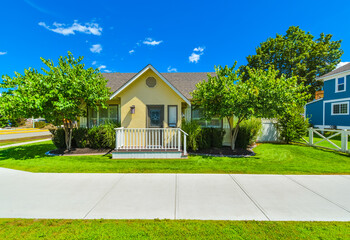 Small yellow family house on sunny day with green lawn and concrete pathway