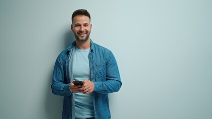 Portrait of happy casual man using phone, Young guy standing at white wall, smiling, Isolated on white background, blank copy space.