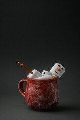 Marshmallow snowman taking hot tub in a red ceramic cup full of cocoa with milk foam. Christmas holidays grey background. Wintertime concept. Hot chocolate with marshmallow and festive decoration.