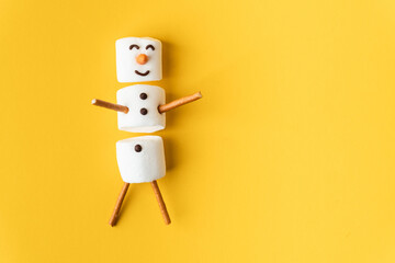 Happy funny marshmallow snowman on the yellow background. Flat lay. Copy space for a free text....