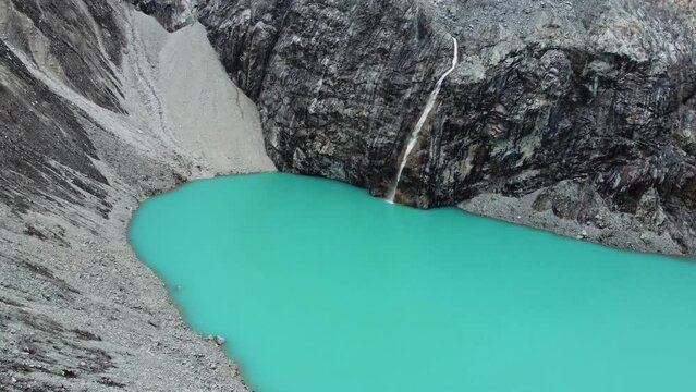 Drone flyover of Laguna 69 (lake 69) or Laguna Sesentinueve, a luminescent green turquoise chemical lake in Peru. Camera flies forwards low over the lake with the glacial waterfall in the background.