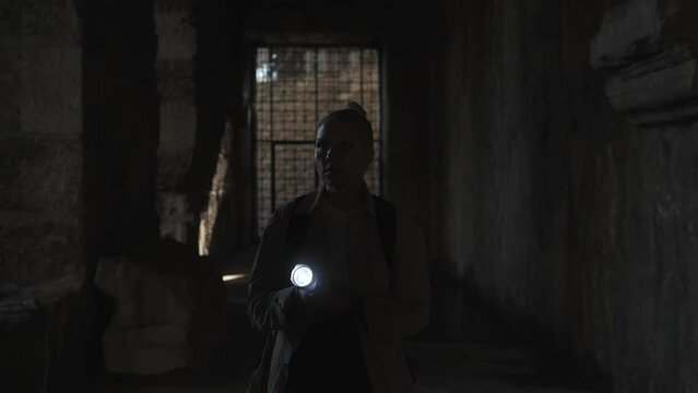 A young female archaeologist walks down a dark corridor to the cell with a flashlight in her hands. High quality 4k footage