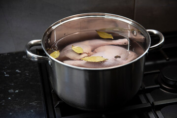 Surowe mięso z kurczaka w wodzie z ziołami w stalowym garnku na czarnej kuchence gazowej