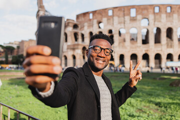 an african takes a selfie in front of the colosseum smiling.