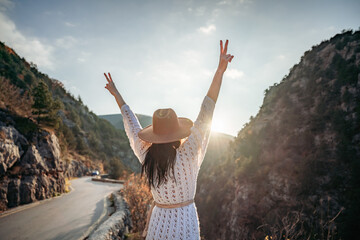 Fototapeta premium Traveler woman in brown hat and white sweater looking at amazing mountains and forest, wanderlust travel concept, atmospheric epic moment
