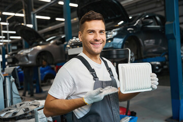 Handsome mechanic showing air filter to camera