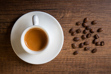 White cup of espresso with coffee beans on wooden table
