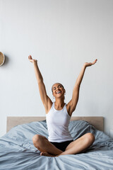 smiling african american woman stretching while sitting on bed in morning.