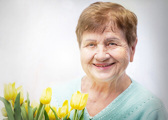 Portret of smiling, positive senior (elderly) woman with bunch of yellow flowers (tulipan). Happy,...
