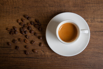 White cup of espresso with coffee beans on wooden table
