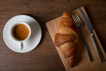 Croissant with espresso in white cup on wooden background 