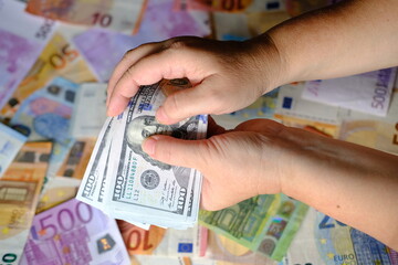 closeup female hands hold american money, count dollars against background of paper euro banknotes, concept of cash, payments, savings, banking, save for vacation, exchange and cashing currency
