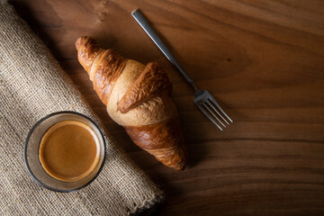Croissant with espresso in white cup on wooden background

