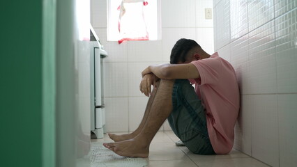 Young man suffering alone at home kitchen floor. miserable person covering face in shame. Negative...