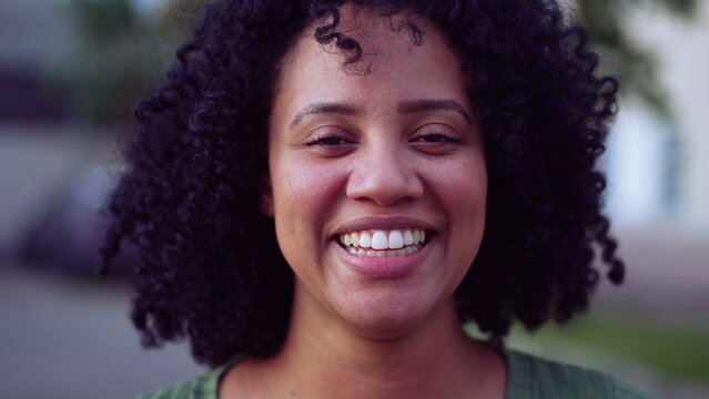 one happy Brazilian black young woman portrait face closeup standing outside looking at camera smiling. African American adult girl female person with joyful emotion