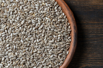 Grey raw sunflower seeds in ceramic bowl on a wooden background, closeup, top view. Purified seeds...