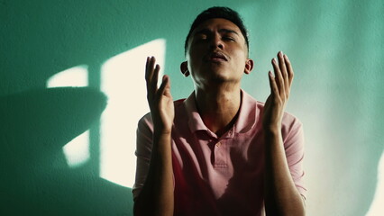 Spiritual young hispanic man praying to God at home. Faithful believer South American male person...