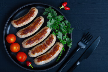 Grilled sausages on pan with herbs and tomato, wood background, closeup