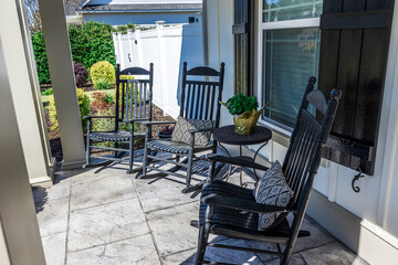 A stamped concrete gray front porch with black rocking chairs sitting in the front for curb appeal