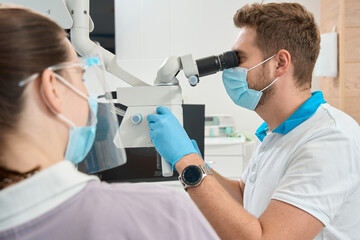 Naklejka na ściany i meble Qualified dentist adjusting modern optical instrument for work