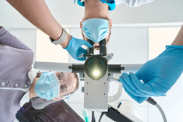 Dentist performing teeth treatment using optical instrument assisted by nurse