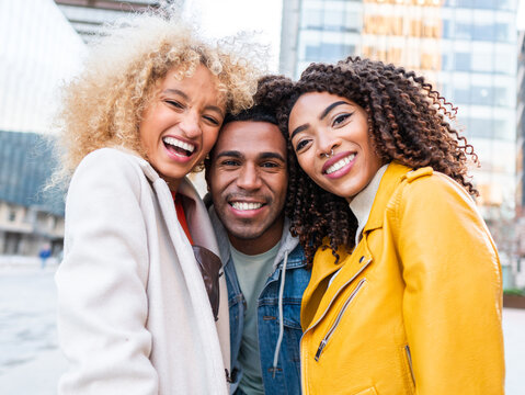 Cheerful multiracial friends smiling and hugging on city square