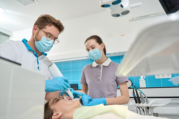 Dental professional examining woman oral cavity with diagnostic device