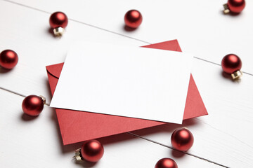 Christmas greeting card mockup with envelope and red balls on white wooden background. Holiday card mockup