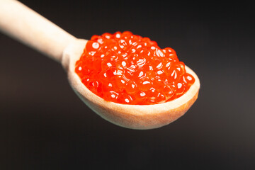 Delicious red caviar in wooden spoon on black background